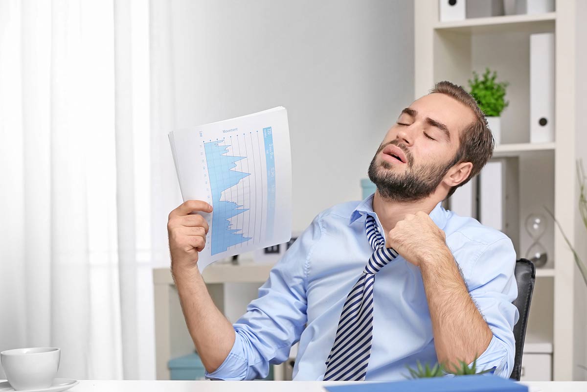 Gestresster Mann im Büro, der sich wegen Hitze Luft zufächelt – Symbolbild für schlechte Raumklimatisierung am Arbeitsplatz