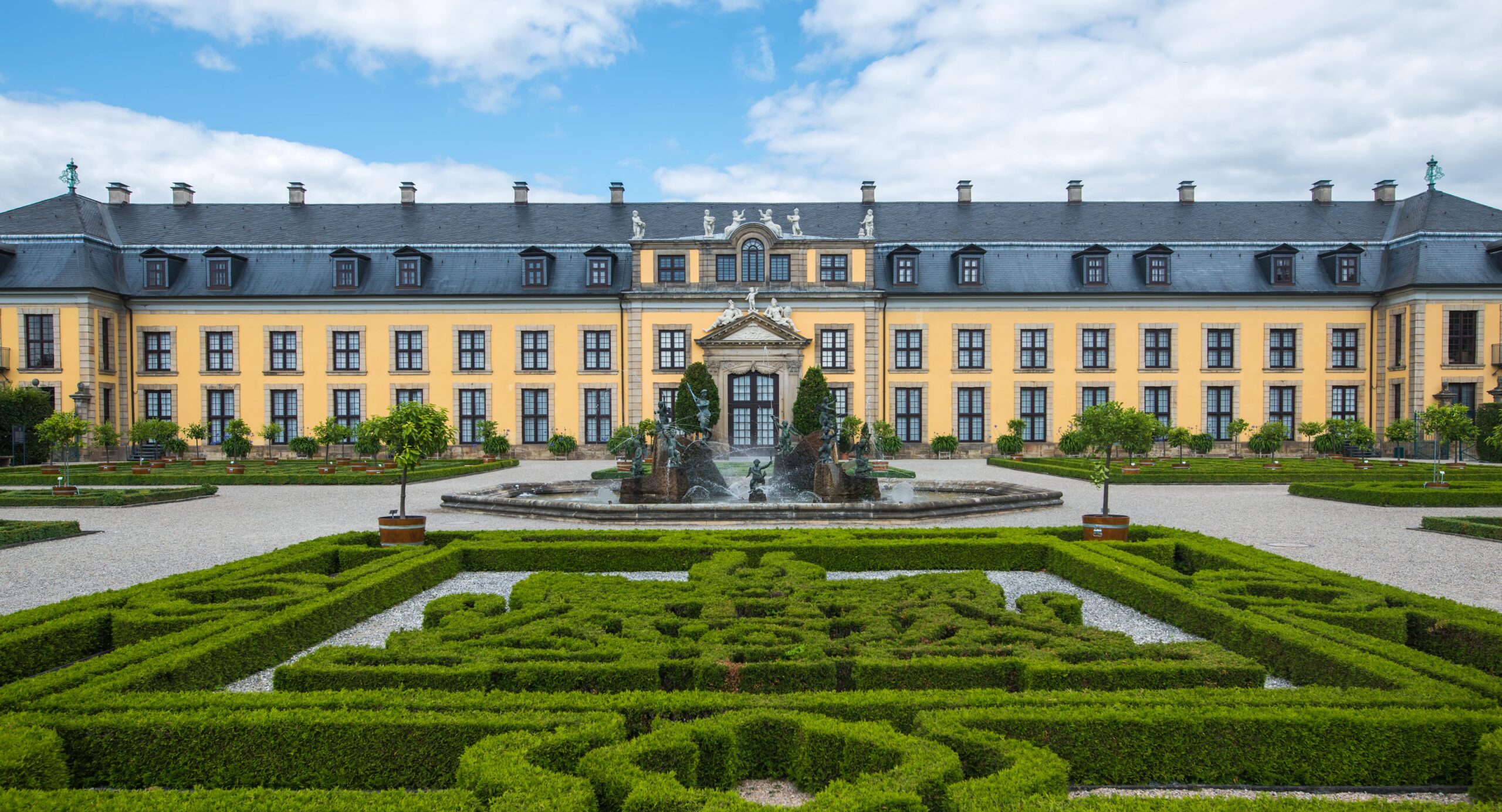 Historisches Schloss mit gepflegtem Garten und Springbrunnen, umgeben von grünen Hecken. Climate Energy.