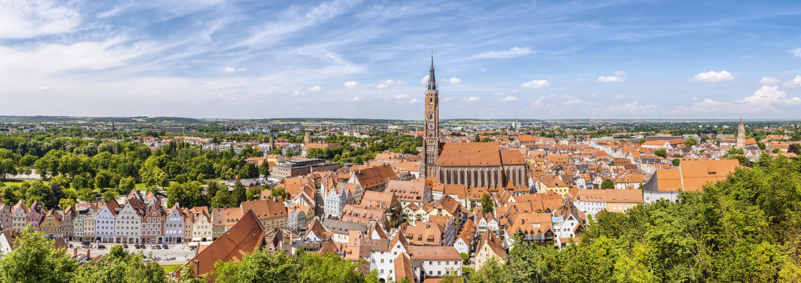 Panoramaaufnahme einer Stadt mit historischen Gebäuden und einem Kirchturm, umgeben von grüner Landschaft. Climate Energy.