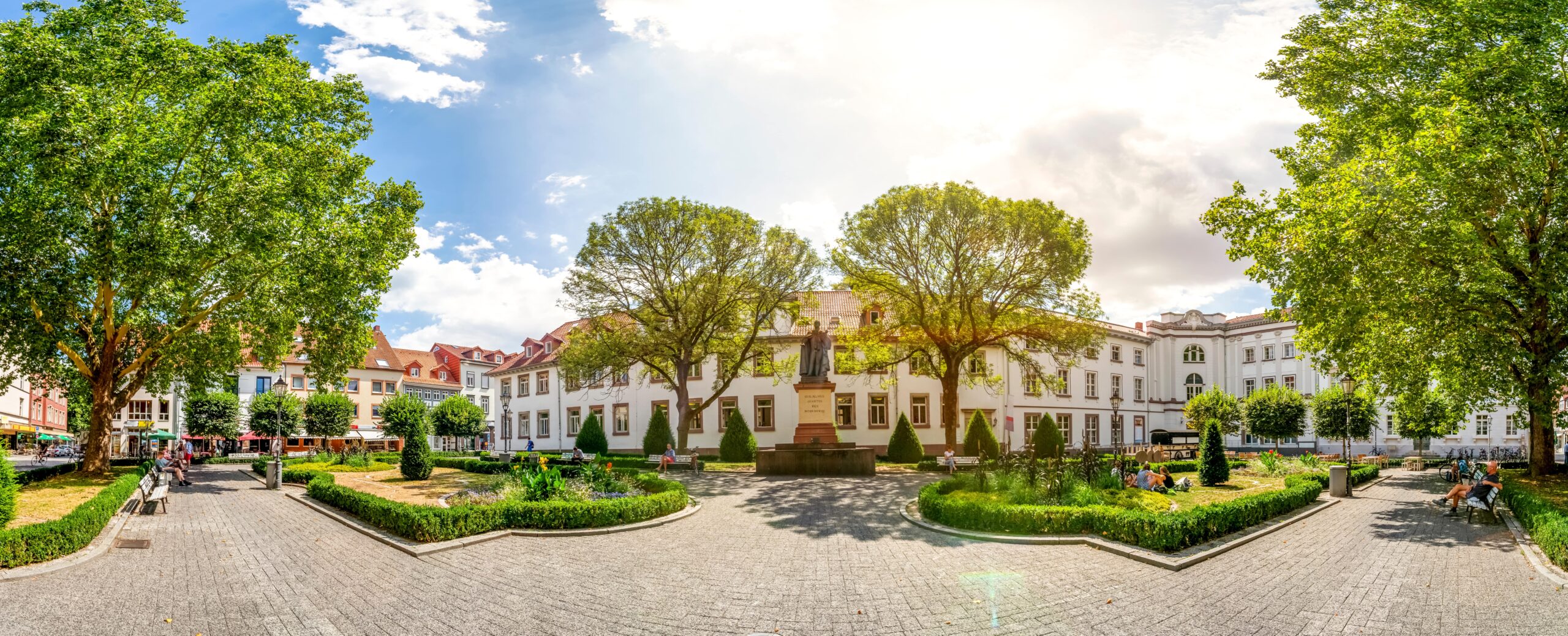 Panoramaansicht eines Platzes mit Bäumen, Grünflächen und einem historischen Gebäude; Thema: Climate Energy.