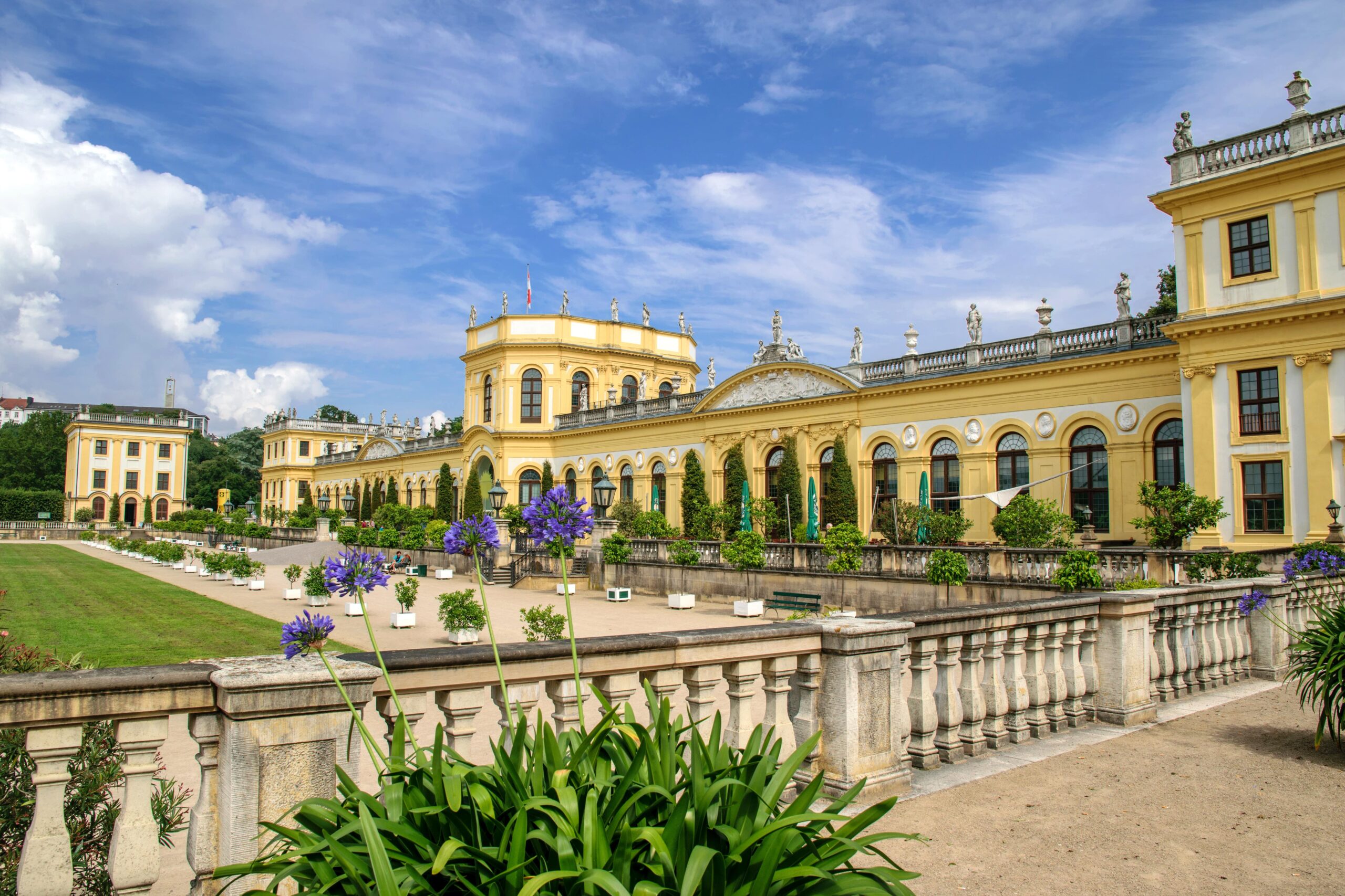 Schloss mit gelber Fassade und Garten, umgeben von Blumen und Bäumen. Klimaenergie als Fokus.