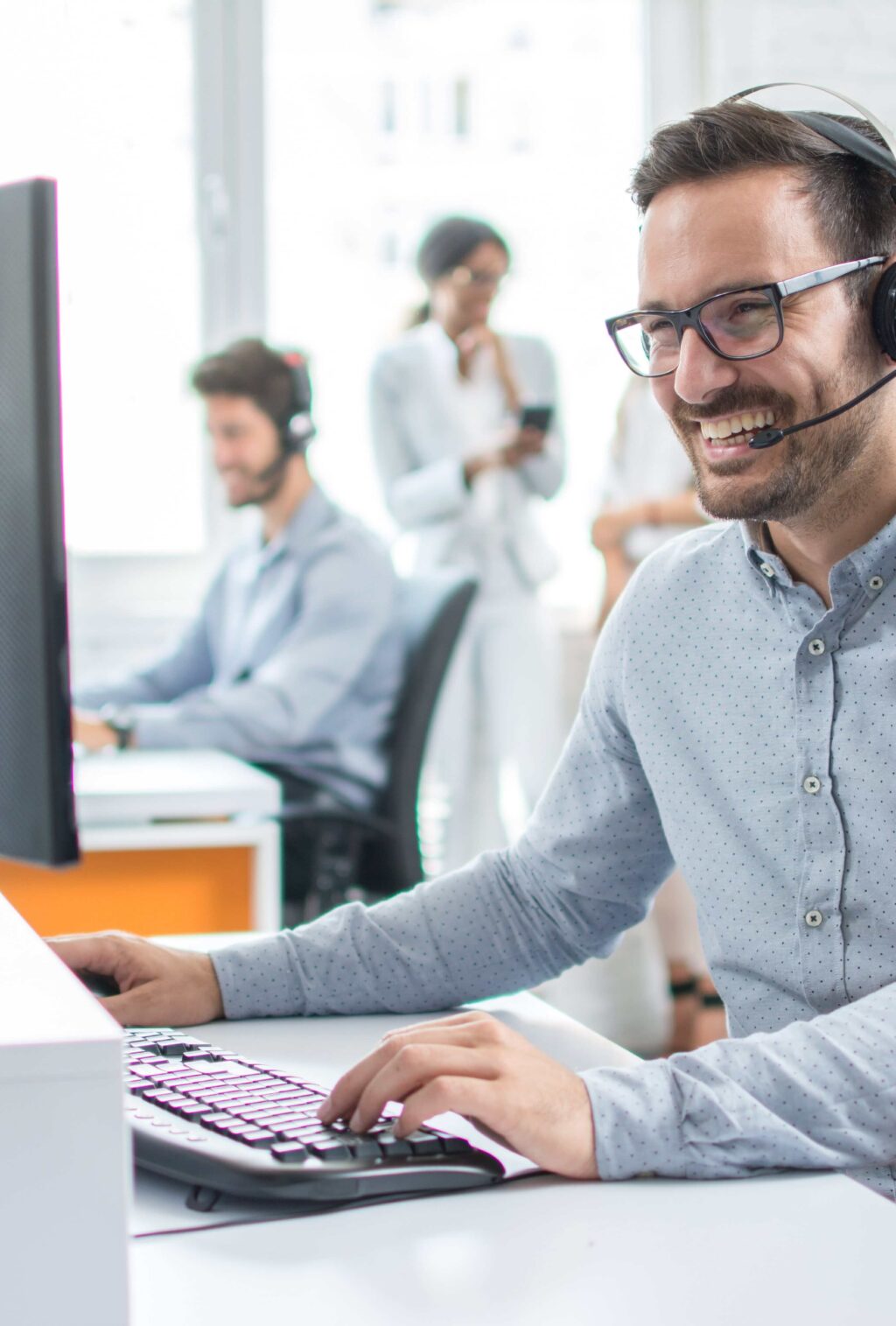 Ein lächelnder Mann mit Kopfhörern arbeitet am Computer in einem modernen Büro. Climate Energy.
