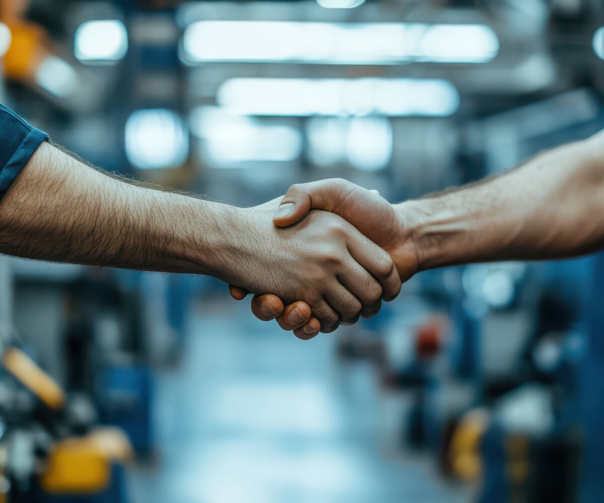 H&auml;ndedruck zwischen zwei Personen in einer Werkstatt, symbolisiert Zusammenarbeit in der Klim energie.